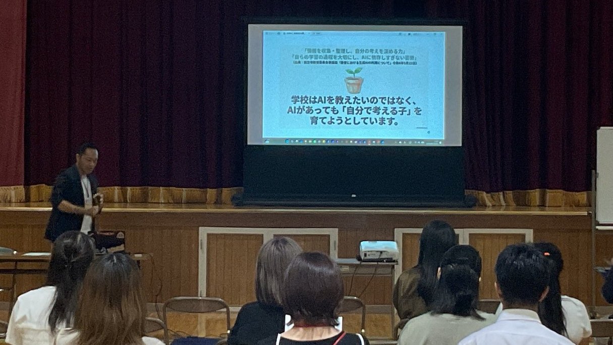 体育館で保護者向けAI講座を行う様子。スクリーンに「学校はAIを教えたいのではなく、AIがあっても自分で考える子を育てようとしています」のスライドが映っている